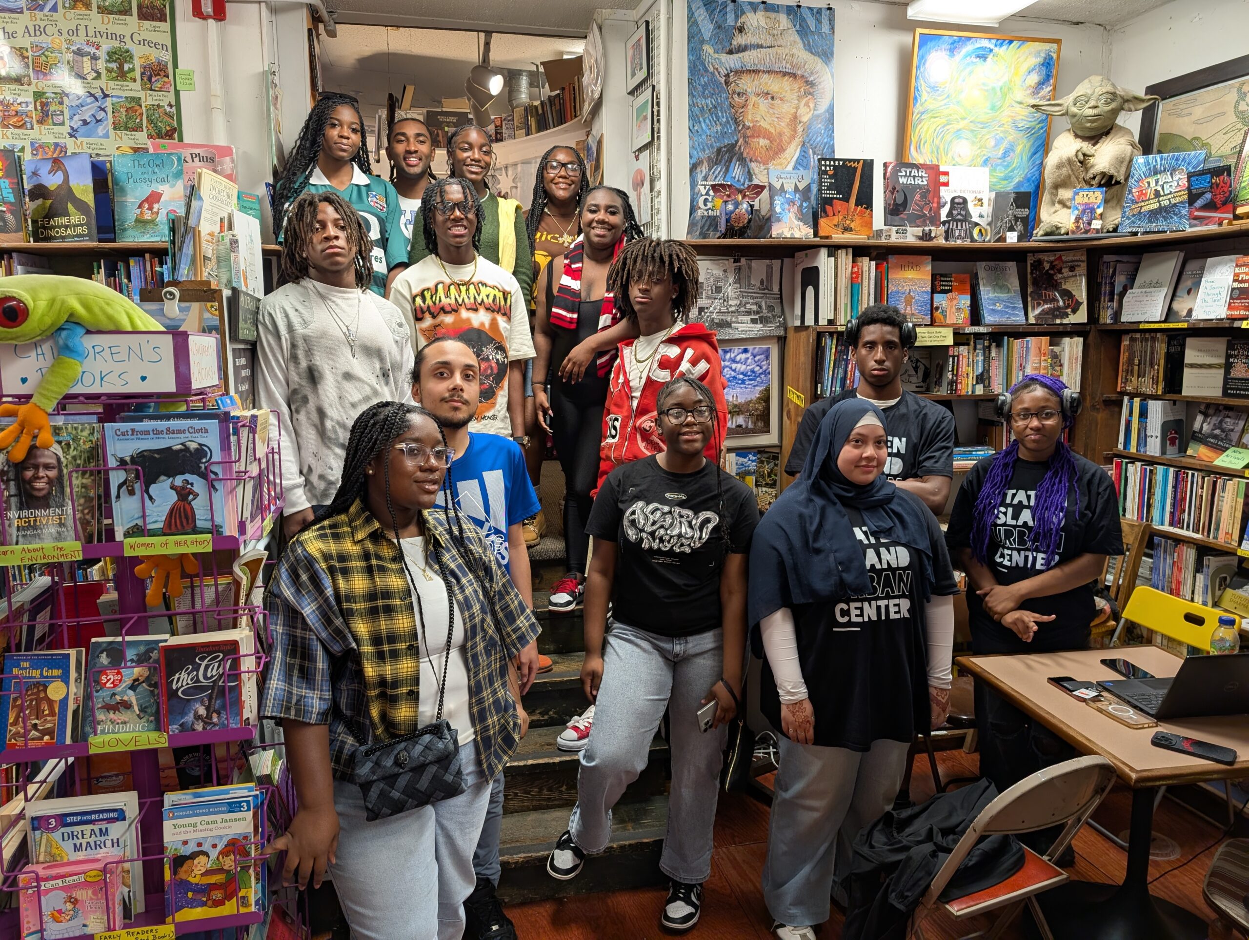 Rear view of three students with braided hair working on Chromebooks at a long black table, displaying reading comprehension or writing exercises.