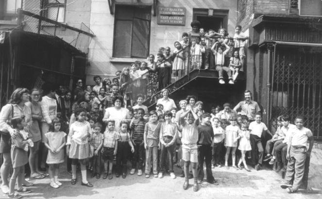 <br />Overhead view of a child's hand working on an "Adding 3 Digits" math worksheet with a pencil, surrounded by numbered wooden blocks on a white table.