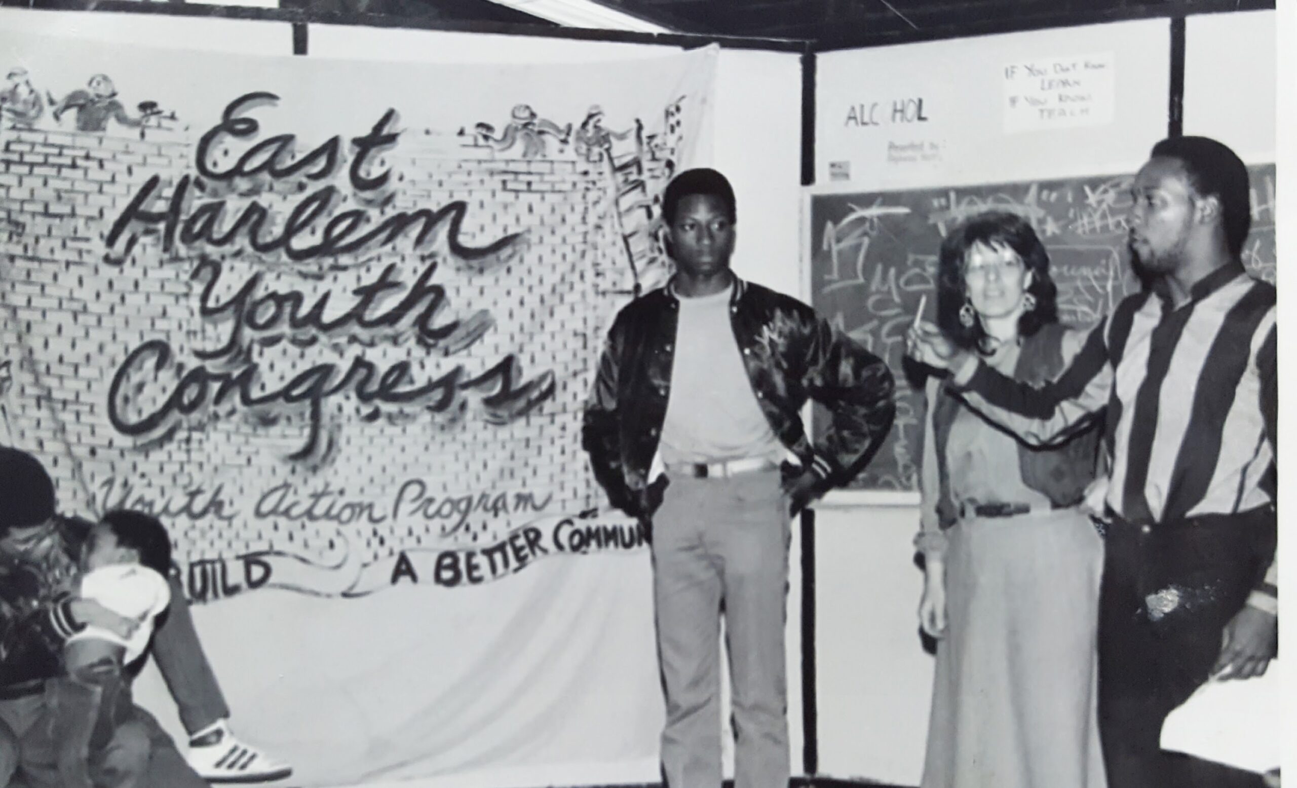 <br />Students participate in an educational activity using laptops, while an adult facilitator stands at a podium displaying the "Quality Life Center" logo in the background.