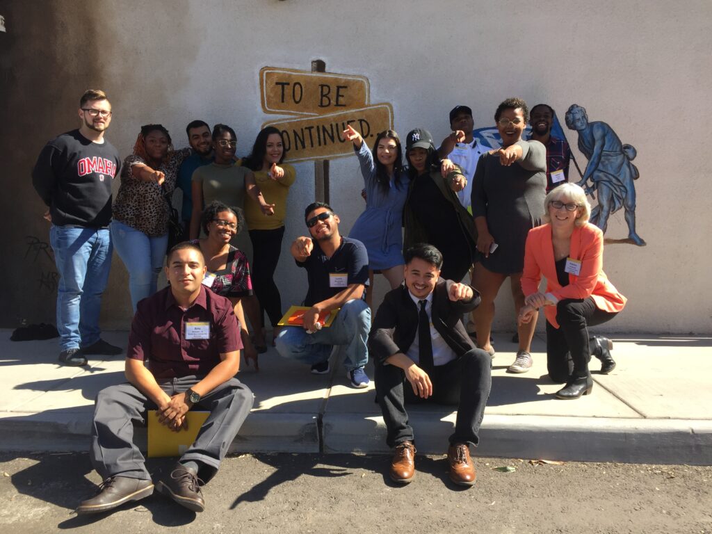 Children in colorful clothing raise their hands during a presentation in a spacious room with screens and an American flag